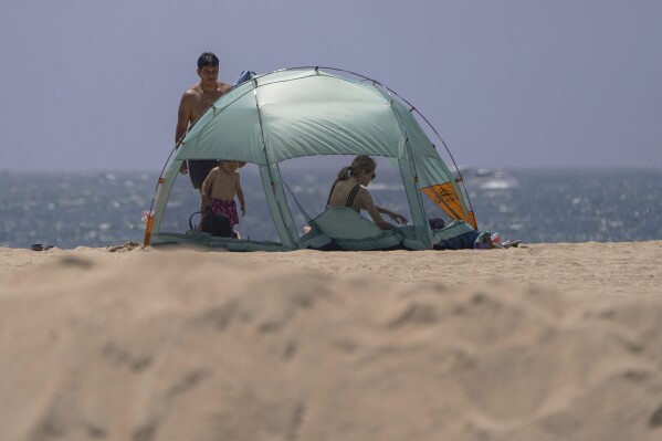 A family sets their beach tent next to a sand berm as winds move in Seal Beach, Calif., Friday, Aug. 18, 2023. Hurricane Hilary is churning off Mexico's Pacific coast as a powerful Category 4 storm threatening to unleash torrential rains on the mudslide-prone border city of Tijuana before heading into Southern California as the first tropical storm there in 84 years. (AP Photo/Damian Dovarganes)