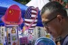 FILE - A man walks by a booth selling foods and beverages displaying planet-shaped flags of China and the U.S. during a spring carnival in Beijing on May 13, 2023. China has detained a worker from a military industrial group on suspicion of spying for the CIA, national security authorities said Friday, Aug. 11, 2023, adding to the list of public accusations of espionage between Beijing and Washington. (AP Photo/Andy Wong, File)