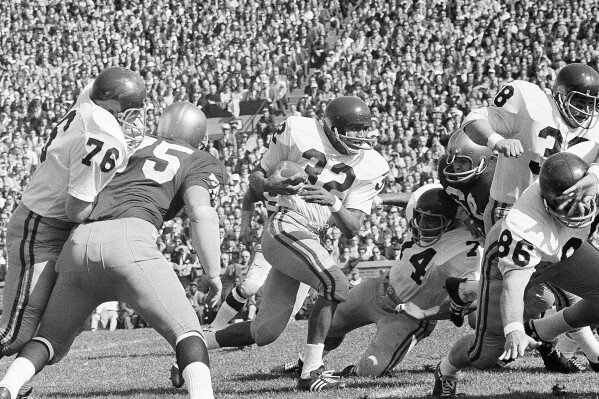 FILE - University of Southern California runningback O.J. Simpson (32) runs against Notre Dame in the first half of an NCAA college football game in South Bend, Ind., Oct. 14, 1967. Blocking for USC are Bob Miller (86), Mike Taylor (74), and Dan Scott (38). O.J. Simpson, the decorated football superstar and Hollywood actor who was acquitted of charges he killed his former wife and her friend but was found liable in a separate civil trial, has died. He was 76. The family announced on Simpson's official X account that he died Wednesday, April 10, 2024, of prostate cancer.(AP Photo/File)