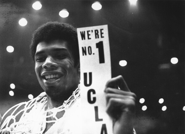 FILE - With a basket net draped over his shoulders, Lew Alcindor, later known as Kareem Abdul-Jabbar, leads UCLA over North Carolina, 78-55, to win the NCAA college basketball championship on March 23 in Los Angeles. Holding a sign after giving victory.  , 1968. (AP Photo/File)