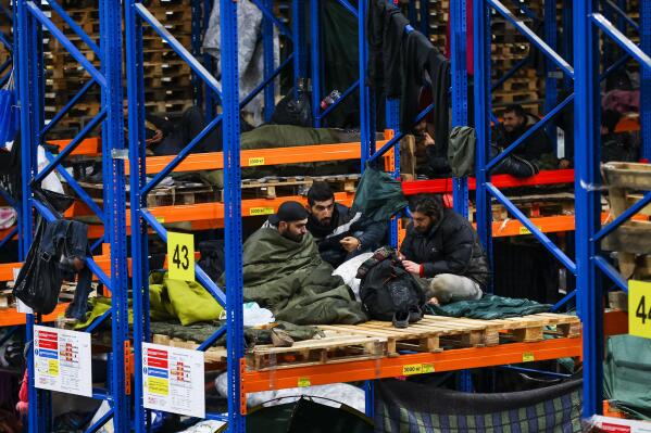Migrants rest inside a logistics center at the checkpoint "Kuznitsa" at the Belarus-Poland border near Grodno, Belarus, Tuesday, Nov. 23, 2021. Belarusian authorities say they have helped more than 100 migrants leave the country on Monday and more are prepared to leave Tuesday, a statement that comes after almost two weeks tensions at on the Belarus' border with Poland, where hundreds of migrants remain stuck. (Andrey Pokumeiko/BelTA via AP)