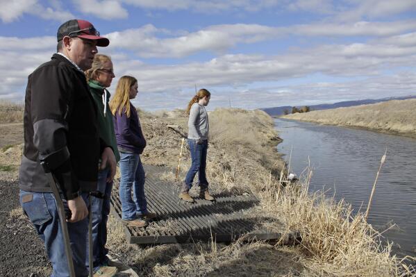 FILE - Farmer Ben DuVal; his wife, Erika, and their daughters, Hannah, 12, in purple, and Helena, 10, in gray, stand near a canal for collecting run-off water near their property in Tulelake, Calif., on March 2, 2020. DuVal inherited the farm from his grandfather, a World War II veteran who won the land by lottery, and worries that plan to demolish four dams on the lower Klamath River could set a precedent for dam removal that could eventually threaten his livelihood. (AP Photo/Gillian Flaccus, File)