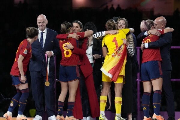 From left, FIFA President Gianni Infantino, Queen Letizia, Spain's Princess Infanta Sofia President of Spain's soccer federation, Luis Rubiales, hug Spain's players the podium following Spain's win in the final of Women's World Cup soccer against England at Stadium Australia in Sydney, Australia, Sunday, Aug. 20, 2023. (AP Photo/Alessandra Tarantino)