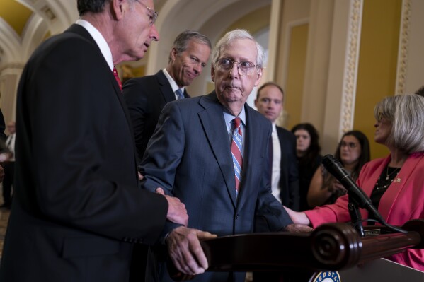 U.S. Senate Minority Leader Mitch McConnell, R-Ky., center, is helped by, from left, Sen. John Barrasso, R-Wyo., Sen. John Thune, R-S.D., and Sen. Joni Ernst, R-Iowa, after the 81-year-old GOP leader froze at the microphones as he arrived for a news conference, Wednesday, July 26, 2023, at the Capitol in Washington. (AP Photo/J. Scott Applewhite)
