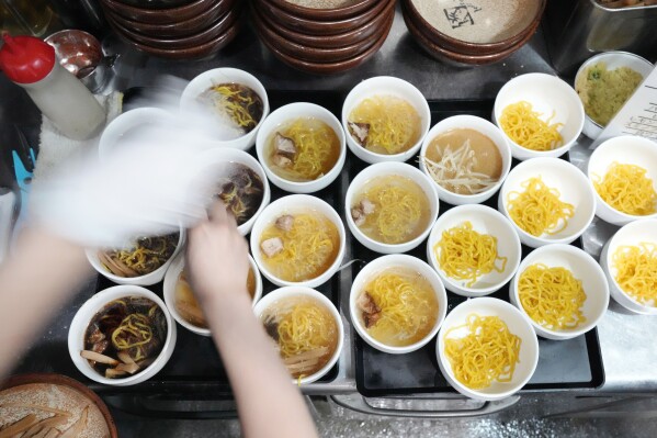 A staff member prepares small bowls of noodle for participants of Tokyo Ramen Tours at Shinbusakiya, a ramen shop which offers "Hokkaido classics," at Shibuya district on April 2, 2024, in Tokyo. (AP Photo/Eugene Hoshiko)