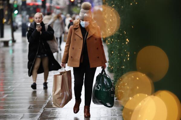Una mujer con cubrebocas carga bolsas de compras mientras camina por Oxford Street el 27 de diciembre de 2021, en Londres. (AP Foto/David Cliff)