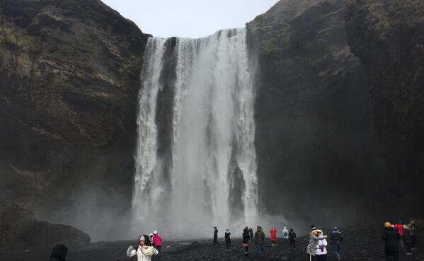 Tourists view the Skogafoss waterfall, southwest of the Myrdalsjokull ice cap that covers the feared Katla volcano, about 34 kilometers (20 miles) west of Vik, Iceland, March 29, 2017.  After a summer of increased seismic activity, seismologists keep watch for volcanic activity, and there's an alert system to warn all 543 residents in Vik if the volcano blows, but there is no system to alert tourists who are flocking to Iceland’s waterfalls and geysers in record numbers.(AP Photo /Sheila Norman-Culp)
