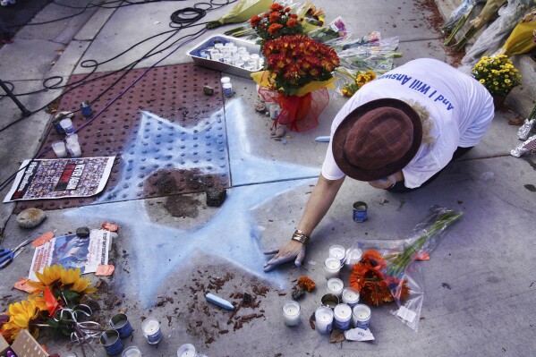 Elena Colombo from Synagogue HAMAKOM chalks a Star of David amongst flowers and candles left at a makeshift shrine placed at the scene of a Sunday confrontation that lead to death of a demonstrator Tuesday, Nov. 7, 2023, in Thousand Oaks, Calif. Paul Kessler, 69, died at a hospital on Monday from a head injury after witnesses reported he was involved in a "physical altercation" during pro-Israel and pro-Palestinian demonstrations at an intersection in Thousand Oaks, a suburb northwest of Los Angeles, authorities said. (AP Photo/Richard Vogel)
