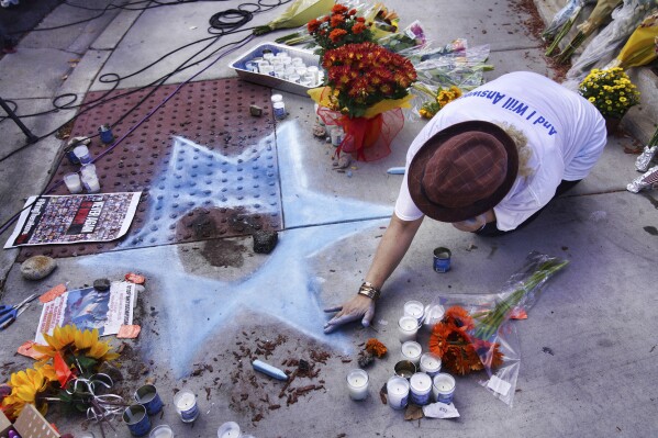 Elena Colombo from Synagogue HAMAKOM chalks a Star of David amongst flowers and candles left at a makeshift shrine placed at the scene of a Sunday confrontation that lead to death of a demonstrator Tuesday, Nov. 7, 2023, in Thousand Oaks, Calif. Paul Kessler, 69, died at a hospital on Monday from a head injury after witnesses reported he was involved in a "physical altercation" during pro-Israel and pro-Palestinian demonstrations at an intersection in Thousand Oaks, a suburb northwest of Los Angeles, authorities said. (AP Photo/Richard Vogel)