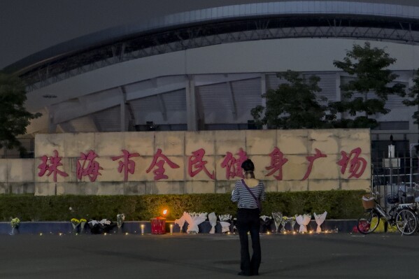 A woman stands near flowers placed outside the "Zhuhai People's Fitness Plaza", where a man deliberately rammed his car into people exercising at the sports center, killing some and injuring others in Zhuhai in southern China's Guangdong province, Nov. 12, 2024. (AP Photo/Ng Han Guan, File)