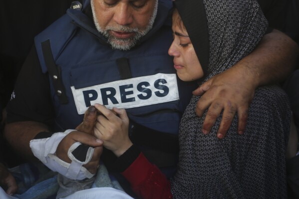 Al Jazeera journalist Wael Dahdouh holds the hand of his son Hamza, who also worked for Al Jazeera and who was killed in an Israeli airstrike in Rafah, Gaza Strip, Sunday, Jan. 7, 2024. Dahdouh lost his wife, two other children and a grandson earlier in the war and was nearly killed himself. (AP Photo/Hatem Ali)