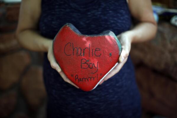 Liz Castleman holds up a rock painted in strawberry colors to honor her son, Charlie, at the Selah Carefarm in Cornville, Ariz., Oct. 4, 2022. Charlie died while under anesthesia during an MRI, likely due to an underlying genetic disorder. Strawberries at the farm have even been forever rebranded as Charlieberries in recognition of his favorite fruit. (AP Photo/Dario Lopez-Mills)