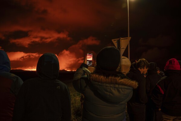 Tourists and visitors try to get a view of the eruption from a distance from the intersection between Reykjanesbraut, Iceland, and the road to Grindavik, Thursday, Aug. 22, 2024. (AP Photo/Marco di Marco)