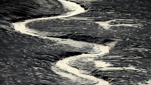 A channel flows through the mud flats along the Seward Highway and Turnagain Arm in Alaska on Oct. 25, 2014. Authorities said, a 20-year-old man from Illinois who was walking Sunday evening, May 21, 2023, on tidal mud flats with friends in an Alaska estuary, got stuck up to his waist in the quicksand-like silt and drowned as the tide came in before frantic rescuers could extract him. (Bob Hallinen/Anchorage Daily News via AP)