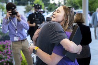 Cobb teacher Katie Rinderle, right, embraces Jack Lakis, a recent Harrison High School graduate, after a Cobb County school board meeting Thursday, Aug. 17, 2023 in Marietta, Ga. . The school board voted to fire Rinderle, who read a book about gender identity to fifth grade students. (Arvin Temkar/Atlanta Journal-Constitution via AP)