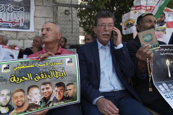 Qadoura Fares, center, attends a protest supporting prisoners, while a fellow protester carries a poster with pictures of the six Palestinian prisoners who escaped from an Israeli jail that says "heroes of the freedom tunnel," in the West Bank city of Ramallah, Tuesday, Sept. 14, 2021. Fares, head of the Prisoners Club, which represents current and former Palestinian prisoners, said they are all “freedom fighters." (AP Photo/Nasser Nasser)