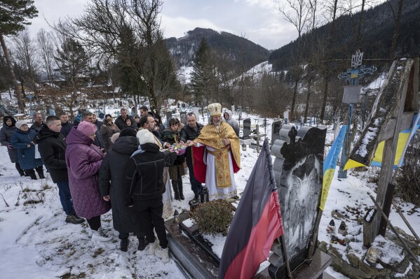Priest Ivan Rybaruk prays with the family of fallen Ukrainian soldier Victor Ivanov at the cemetery during Christmas celebration in Kryvorivnia village, Ukraine, Sunday, Dec. 24, 2023. Ivanov was killed by Russian armed forces near Bakhmut on October 2022. (AP Photo/Evgeniy Maloletka)