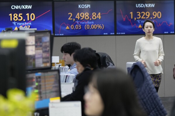 A currency trader passes by the screens showing the Korea Composite Stock Price Index (KOSPI), center, and the foreign exchange rate between U.S. dollar and South Korean won, right, at the foreign exchange dealing room of the KEB Hana Bank headquarters in Seoul, South Korea, Wednesday, Jan. 31, 2024. Asian stocks mostly declined Wednesday as markets awaited a decision on interest rates by the Federal Reserve, while China reported manufacturing contracted in January for a fourth straight month.(AP Photo/Ahn Young-joon)