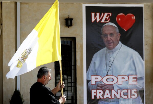 A Christian priest holds a Vatican flag as he walks by a poster of Pope Francis during preparations for the Pope's visit in Mar Youssif Church in Baghdad, Iraq, Friday, Feb. 26, 2021. (AP/Photo/Hadi Mizban)