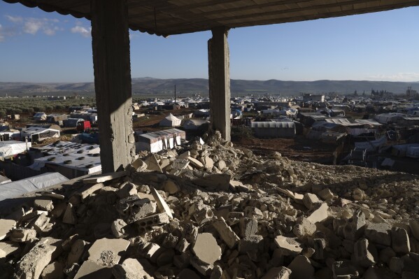 A house damaged in the February 2023 earthquake overlooks the tents of Syrians displaced by it in Jinderis, Syria, on Jan. 27, 2024. (AP Photo/Omar Albam)