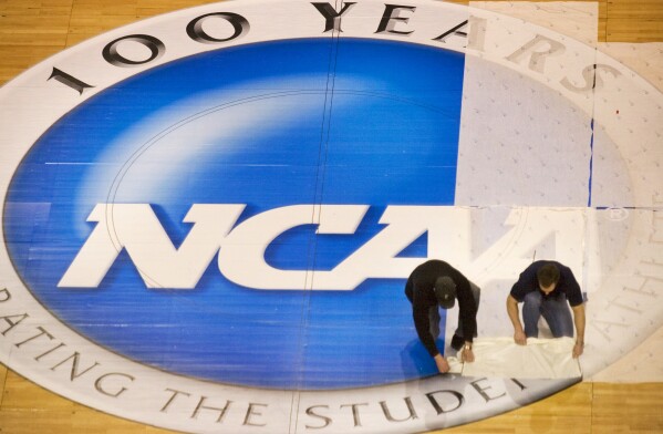 FILE - Wachovia Center operations manager Jim McDonald, left, and carpenter foreman Tim Allen remove the protective film covering the NCAA logo at mid-court on the center's basketball court, Wednesday, March 15, 2006, in Philadelphia. NCAA athletes will be immediately eligible to play no matter how many times they transfer — as long as they meet academic requirements — after the association fast-tracked legislation Wednesday, April 17, 2024, to fall in line with a recent court order. (Ed Hille/The Philadelphia Inquirer via AP, FIie)