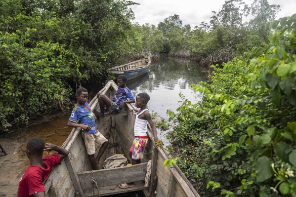 Children sit inside a fishing boat outside a mangrove in Kimpozia village, one of the areas auctioned for oil drilling, in Moanda, Democratic Republic of the Congo, Monday, Dec. 25, 2023. Its government is auctioning off 30 oil and gas blocks around the country. (AP Photo/Mosa'ab Elshamy)