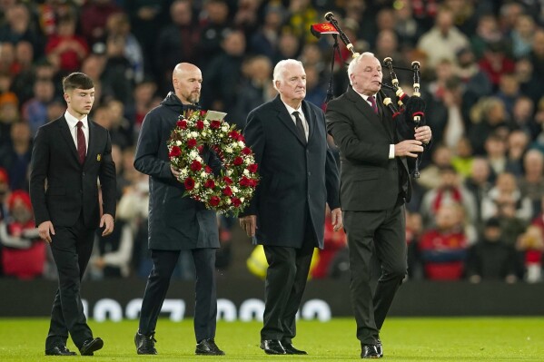 Manchester United's head coach Erik ten Hag, second left, with Alexander Stepney English former player, second right, and Manchester United academy player Dan Gore lays flowers in memory of Sir Bobby Charlton prior the Champions League group A soccer match between Manchester United and Copenhagen at the Old Trafford stadium in Manchester, England, Tuesday, Oct. 24, 2023. (AP Photo/Dave Thompson)