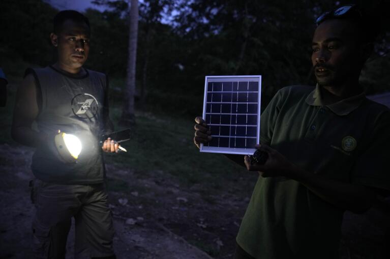Antonius Makambombu, right, a worker of Sumba Sustainable Solutions demonstrates to villagers how a solar panel lamp works in Ndapayami village on Sumba Island, Indonesia, Monday, March 20, 2023. Working with international donors to help subsidize the cost, it provides imported home solar systems, which can power light bulbs and charge cellphones, for monthly payments equivalent to $3.50 over three years. (AP Photo/Dita Alangkara)