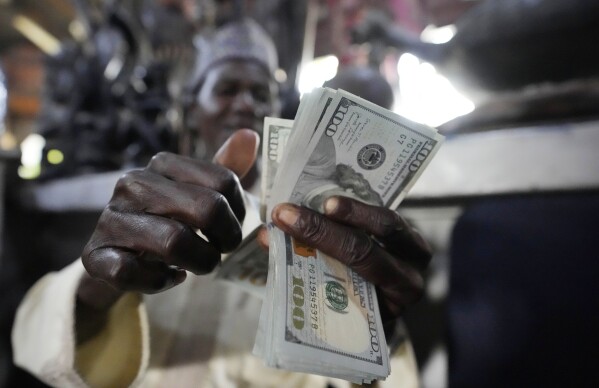 A man counts U.S. $100 bills at the craft and art market in Lagos, Nigeria, on Wednesday, Aug. 16, 2023. Across the developing world, many countries are fed up with America's dominance of the global financial system — and especially the power of the dollar. (AP Photo/Sunday Alamba)