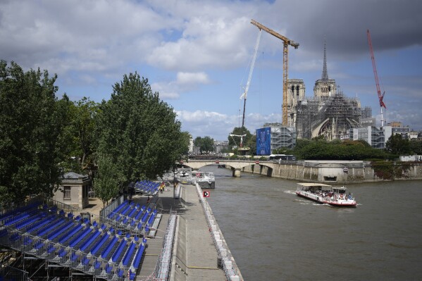 A tourists boat makes its way on the Seine river with stands installed on its banks, Thursday, July 4, 2024 by Notre Dame de Pari cathedral in Paris. The Seine river will host the Paris Olympic Games opening ceremony on July 26. (AP Photo/Thibault Camus)