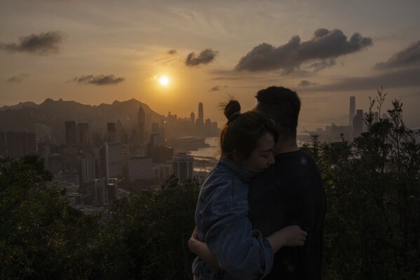 FILE - Visitors look at sunset from a hill in Hong Kong, Friday, March 22, 2024. Two weeks after Hong Kong introduced a new national security law, life in the city appears unchanged. A 2020 law drew thousands of protesters to the streets when it was enacted. Now, that's seen as too risky.(AP Photo/Louise Delmotte, File)