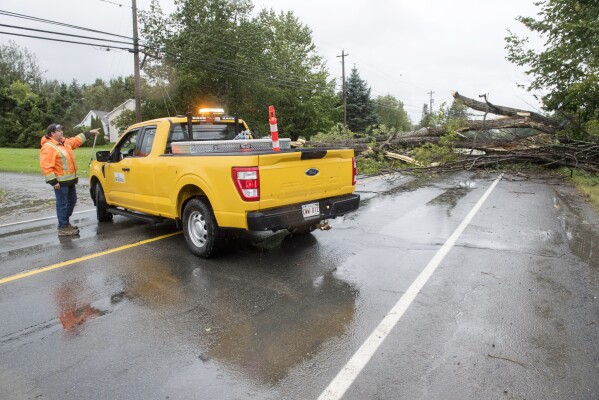 Personnel with the New Brunswick department of transportation and infrastructure block the road next to a large tree that fell on Woodstock Road in Fredericton, N.B., on Saturday, Sept. 16, 2023. (Stephen MacGillivray /The Canadian Press via AP)