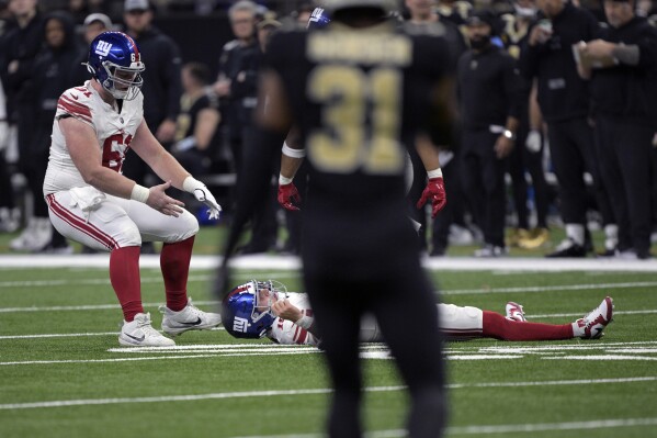 New York Giants quarterback Tommy DeVito is assisted by teammate John Michael Schmitz Jr., left, after being hit during the first half of an NFL football game against the New Orleans Saints Sunday, Dec. 17, 2023, in New Orleans. (AP Photo/Matthew Hinton)