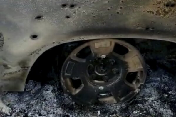 This frame from Nov. 4, 2019, video by Kenny Miller and posted on the Twitter account of Alex LeBaron shows a burned-out vehicle that was being used by some members of the LeBaron family as they were driving in a convoy near the Sonora-Chihuahua state border in Mexico. Mexican authorities say drug cartel gunmen ambushed multiple vehicles, including this one, slaughtering several women and children. (Kenny Miller/Courtesy of Alex LeBaron via AP)