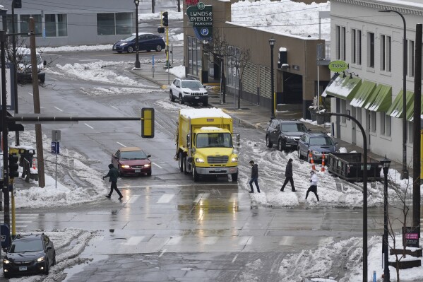 Pedestrians crosses the street as snow partially covers the roads, Monday, March 25, 2024, in Minneapolis. (AP Photo/Abbie Parr)