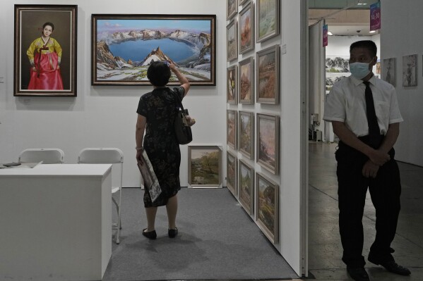 A security guard stands watch as a visitor takes a photo of a painting depicting snow-capped Mount Baekdu, the mythical birthplace of the Korean people, at the booth for The Paintings Say Arirang gallery that trumpets itself as China's premier seller of North Korean art, in Beijing, Sept. 8, 2023. The gallery's existence and conspicuous sales tactics, experts say, highlight China's lax enforcement of U.N. sanctions targeting North Korea to stymie Pyongyang's nuclear program. (AP Photo/Ng Han Guan)
