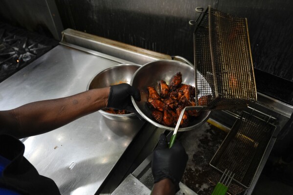 A line cook places chicken wings into a bowl before serving, Wednesday, June 12, 2024, at a barbecue restaurant in Cincinnati. Psychologists have known for years now that men tend to eat more meat than women, but a study of people around the world now reveals that that's true across cultures. (AP Photo/Joshua A. Bickel)