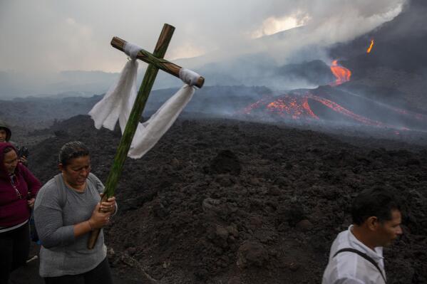 A woman carries a cross during a pilgrimage to pray that the Pacaya volcano decreases its activity in San Vicente Pacaya, Guatemala, Wednesday, May 5, 2021. The volcano, just south of the capital, has been active since early February. (AP Photo/Moises Castillo)
