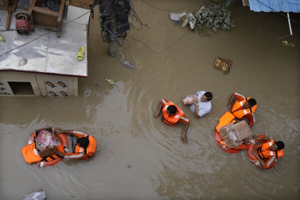 FILE - National Disaster Response Force (NDRF) personnel distribute relief material to flood affected people stuck in a low lying area around the river Yamuna in New Delhi, India, July 14, 2023. At about summer's halfway point, the record-breaking heat and weather extremes are both unprecedented and unsurprising, hellish yet boring in some ways, scientists say. (AP Photo/Manish Swarup, File)