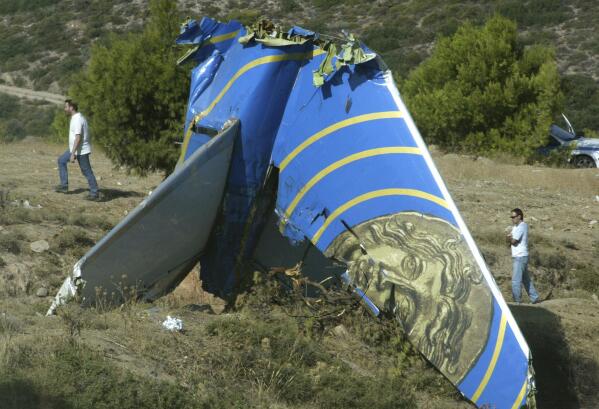 FILE - Police officers walk behind the tail of the crashed Cypriot Helios plane on a hillside in Grammatiko, 40 kilometers (25 miles) north of Athens, Greece, Aug. 22, 2005. Some aviation experts are citing pilot hypoxia as a leading theory for why an unresponsive business plane flew over the nation’s capital Sunday, June 4, 2023, and caused the military to scramble fighter jets. Greek investigators said pilots on a Cypriot airliner did not realize an automatic pressurization system was set to “manual” when a loss of cabin pressure and oxygen led to hypoxia and the plane’s crash in Greece in 2005, killing all 121 people on board. (AP Photo/Petros Giannakouris, File)