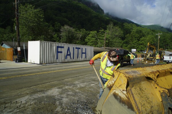 David Cruz mixes cement in the bucket of an end loader for a sewer manhole on Main Street in Chimney Rock Village, N.C., on Wednesday, May 14, 2025. (AP Photo/Allen G. Breed)