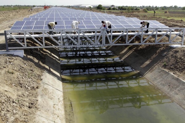 FILE - Indian workers give finishing touches to installed solar panels covering the Narmada canal at Chandrasan village, outside Ahmadabad, India, Sunday, April 22, 2012. The project brings water to hundreds of thousands of villages in the dry, arid regions of western India’s Gujarat state. (AP Photo/Ajit Solanki, File)