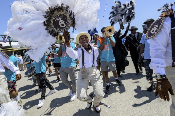 Members of the Zulu Steppers parade with the New Groove Brass Band along the Fair Grounds at the New Orleans Jazz and Heritage Festival in New Orleans, Thursday, April 25, 2024. (AP Photo/Matthew Hinton)