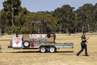 A police officer walks past a trailer with a hot-air balloon basket on it after the discovery of a man's body at Yarra Bend Park in Melbourne, Monday, March 18, 2024. A man has fallen to his death from a hot-air balloon as it passed over suburban Melbourne, Australia's second largest city. (Diego Fedele/AAP Image via AP)