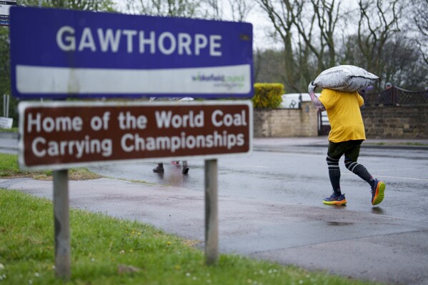 A contestant carrying a 50kg sack of coal passes a road sign at the World Coal Carrying Championships in Ossett, West Yorkshire, England, Monday, April 21, 2025. (AP Photo/Jon Super)