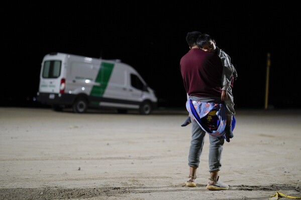 FILE - A man from Colombia holds his son as he waits to apply for asylum after crossing the border from Mexico, Tuesday, July 11, 2023, near Yuma, Ariz. Immigration advocates may file a lawsuit alleging that an online appointment system at border crossings fails to meet U.S. obligations to make asylum available to people fleeing persecution, the latest legal challenge to the Biden administration's border policies. (AP Photo/Gregory Bull, File)