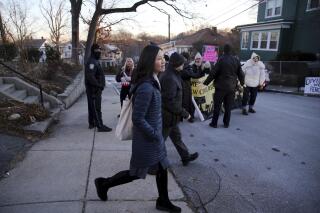 FILE - Boston Mayor Michelle Wu passes a small group of demonstrators as she leaves her home in the Roslindale neighborhood of Boston, Jan. 26, 2022. The group was protesting the vaccine mandate in Boston. Wu, who has been targeted in early mornings by people outside her home protesting her city employee coronavirus vaccine mandate, filed an ordinance Monday, Feb. 28, 2022, that would limit when protesters can picket. (Craig F. Walker/The Boston Globe, File)