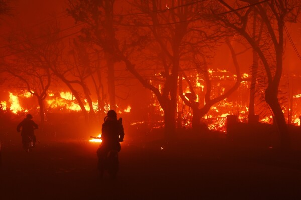 Two people ride by on motorcycles as the Palisades Fire destroys an area in the Pacific Palisades neighborhood of Los Angeles, Tuesday, Jan. 7, 2025. (AP Photo/Etienne Laurent)