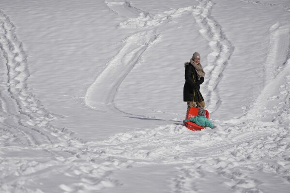 Megan Quinn pulls her daughter Zoe up a hill as they sled Tuesday, Jan. 16, 2024, in Nashville, Tenn. While the U.S. is shivering through bone-chilling cold, most of the rest of world is feeling unusually warm weather. Scientists Tuesday say that fits with what climate change is doing to Earth. (AP Photo/George Walker IV)