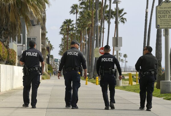 FILE - In this March 28, 2020, file photo, Los Angeles police officers patrol a sparsely populated Venice Beach boardwalk in Los Angeles. At least three police officers in California have died so far from COVID-19 and officers have been urged to wear masks when they are interacting with the public. (AP Photo/Mark J. Terrill, File)
